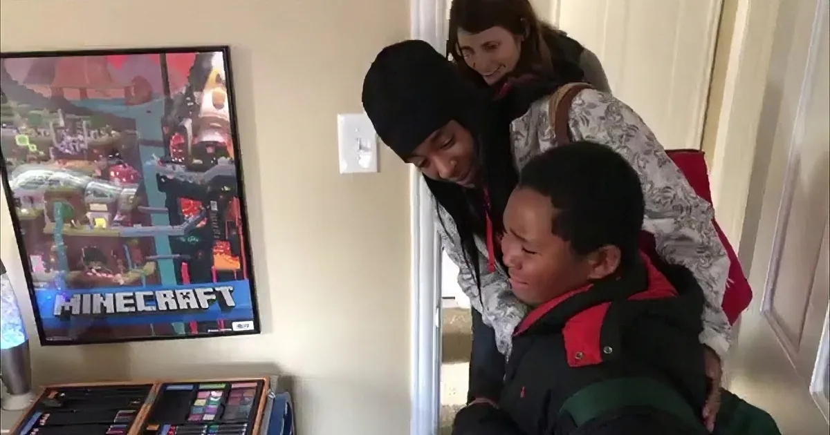 A person in a black hoodie leans over a child in a red and black jacket, both looking at a computer screen with a...