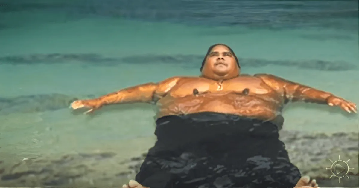 A person is lying on a beach with arms outstretched, wearing black pants and a tan body.