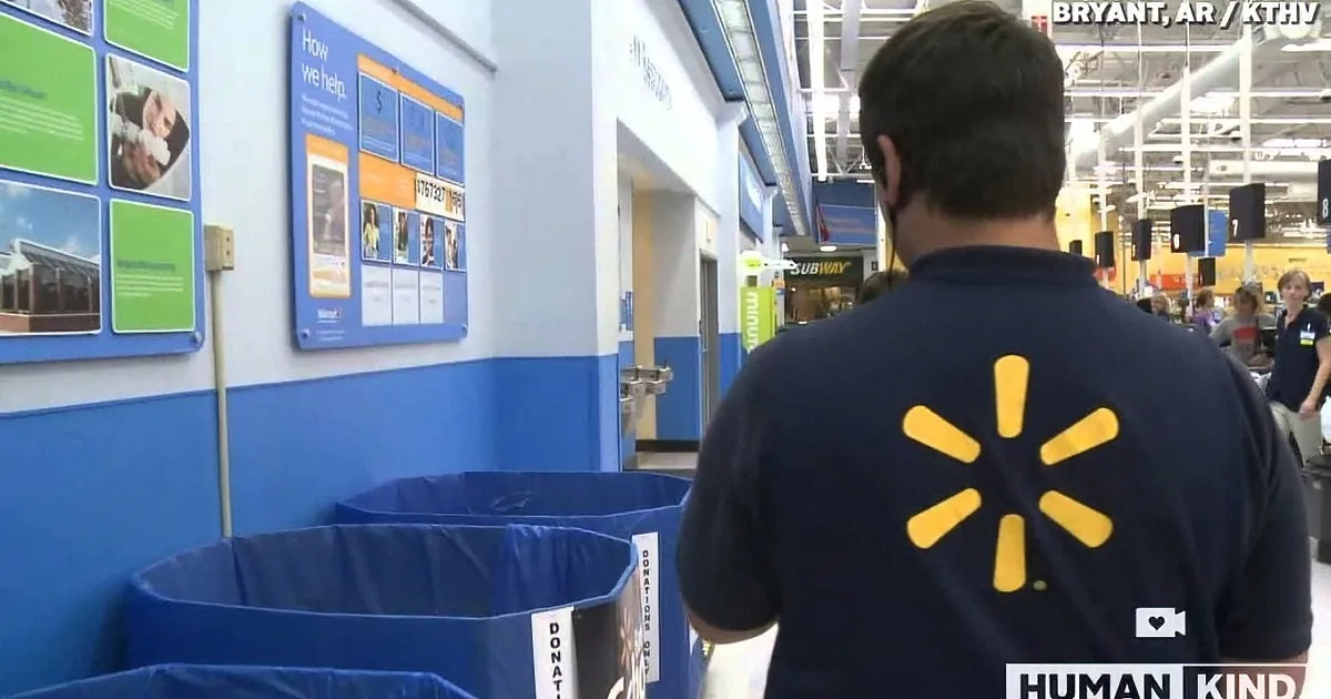 A Walmart employee in a blue shirt with the Walmart logo walks near donation bins in a store.
