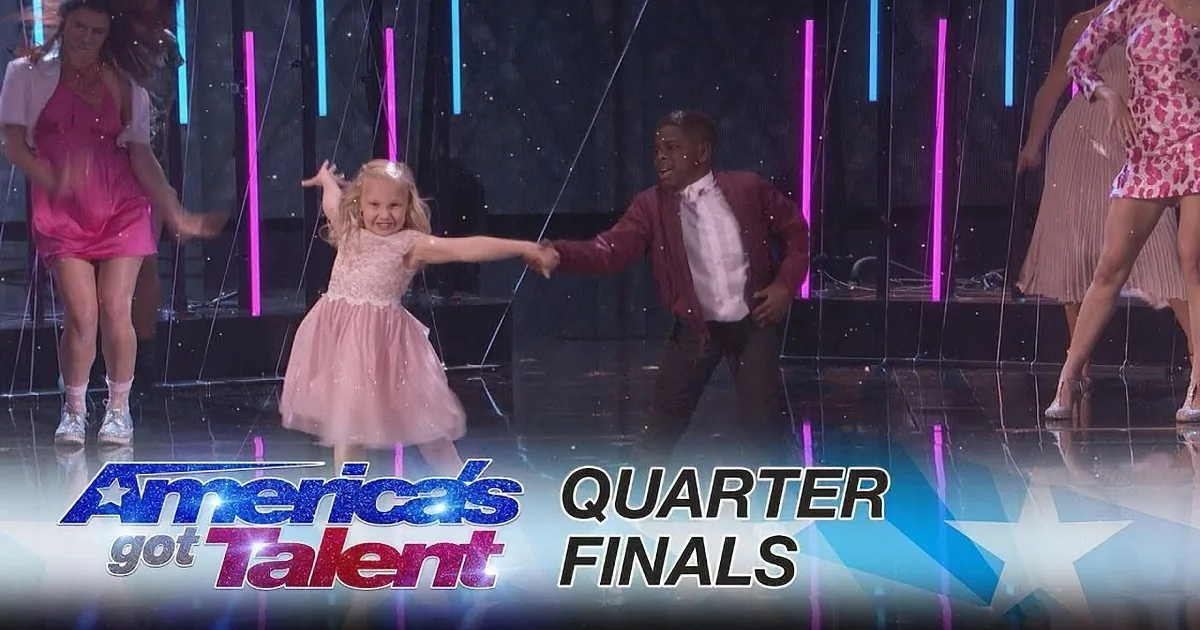 A young girl in a pink dress dances joyfully with a boy in a maroon jacket on stage at America's Got Talent Quarter Finals.