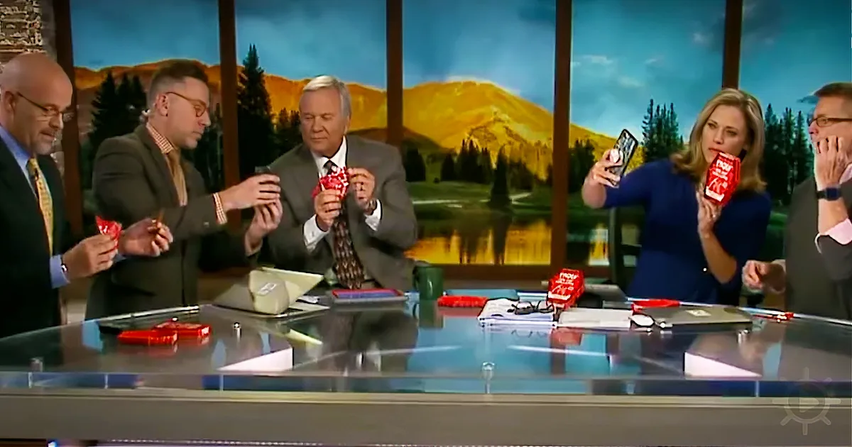 A news panel discusses a topic, with one person holding a red object and others looking at their phones.