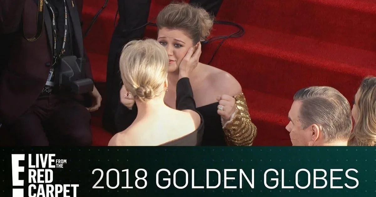 A woman in a black dress adjusts her hair on the red carpet at the 2018 Golden Globes.