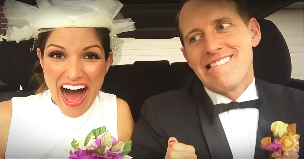 A bride and groom in wedding attire smile and laugh in a car.