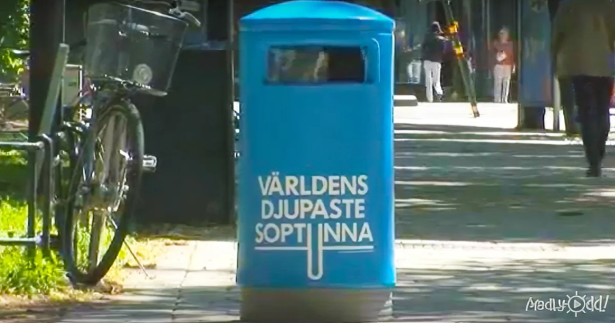 A blue trash bin labeled "Världens Djupaste Soptunna" stands on a sidewalk near a bicycle.
