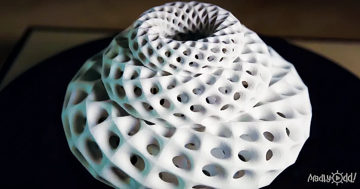 A 3D-printed object with a honeycomb-like structure and a central hole is displayed against a dark background.
