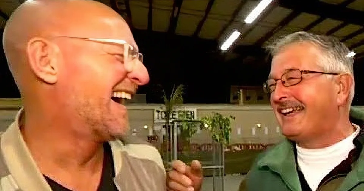 A man with glasses and a bald head is laughing, surrounded by other smiling individuals in a casual setting.