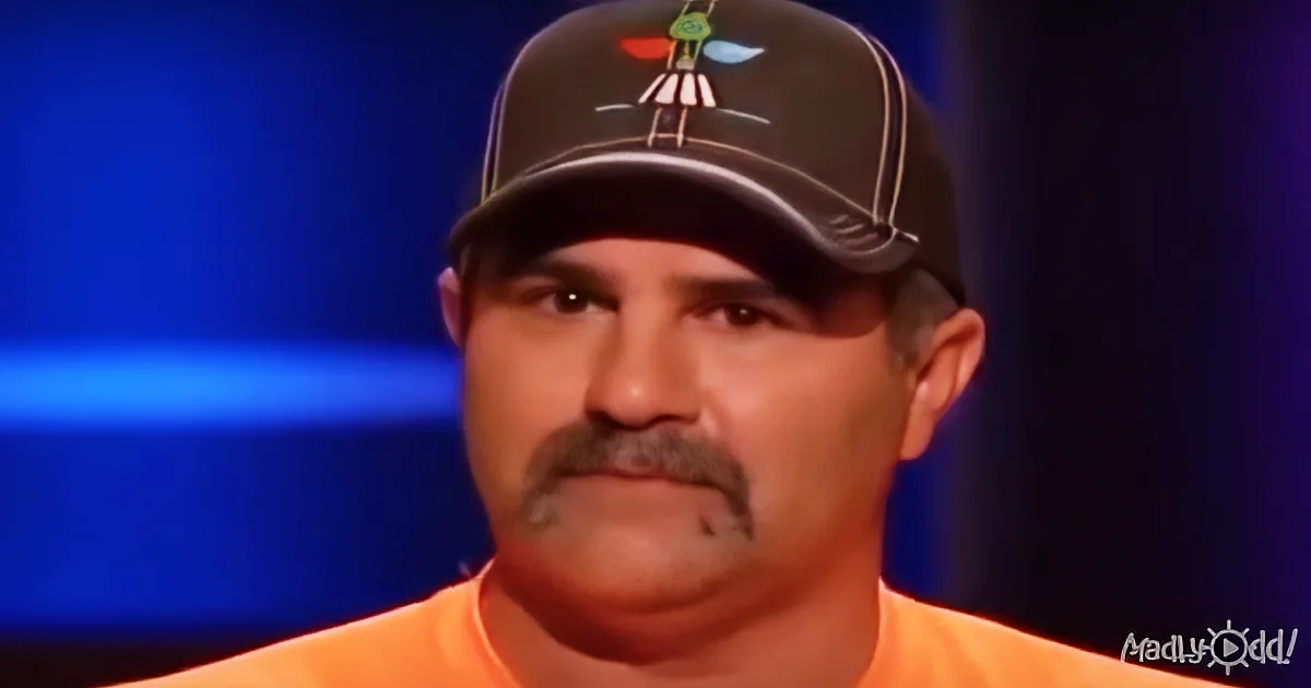 A man wearing an orange shirt and a black cap with colorful designs is shown in a close-up.