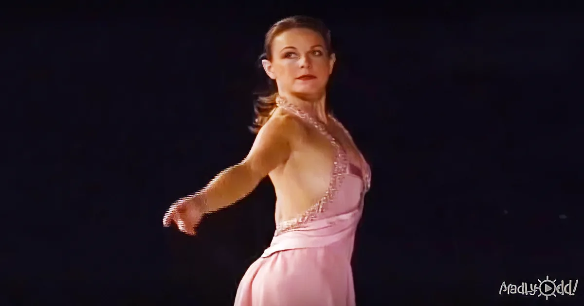 A woman in a pink dress with a halter neck is dancing gracefully against a dark background.
