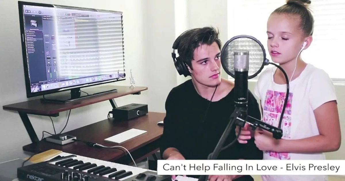 A young man and girl record "Can't Help Falling In Love" by Elvis Presley in a home studio setup.
