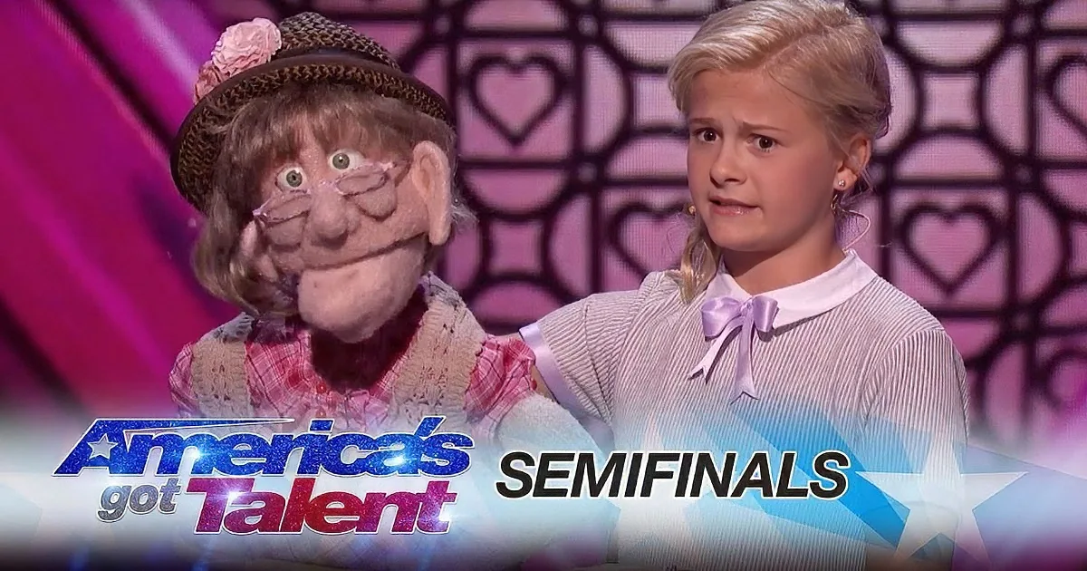 A young girl in a pink dress stands beside a puppet on stage at America's Got Talent semifinals.