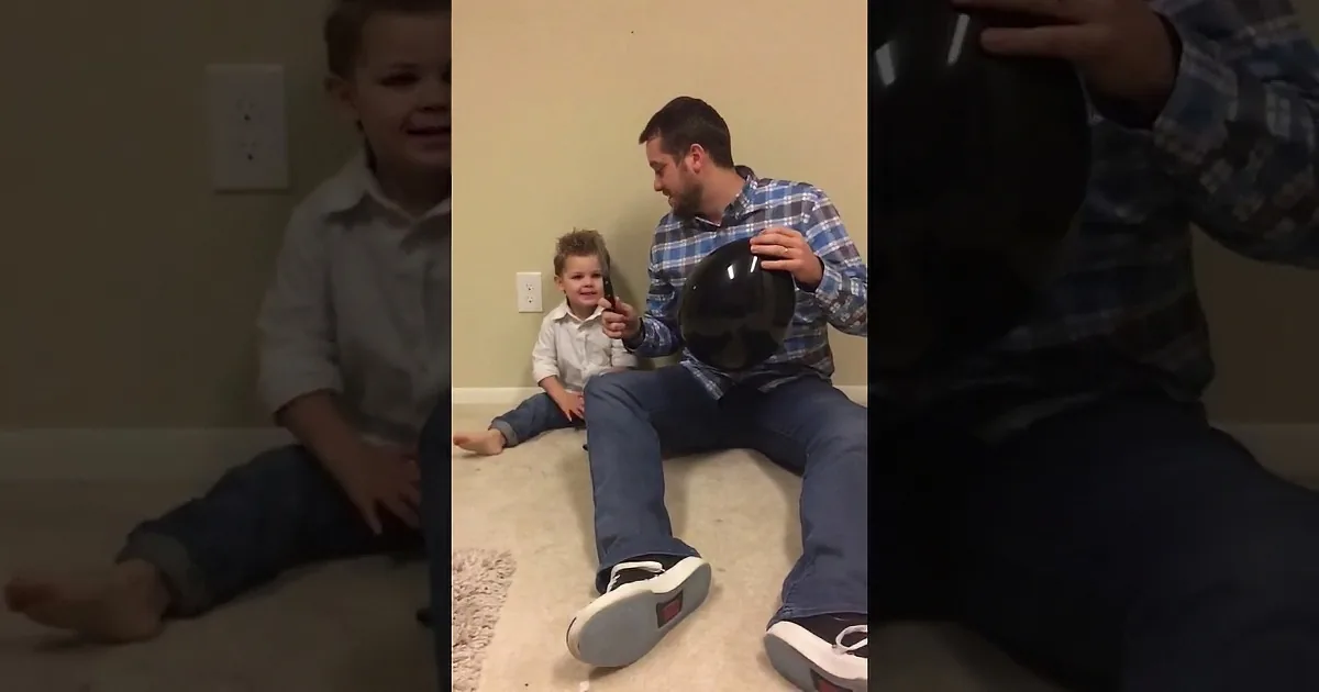 A man and two children sit on the floor, the man holding a black object and a phone.