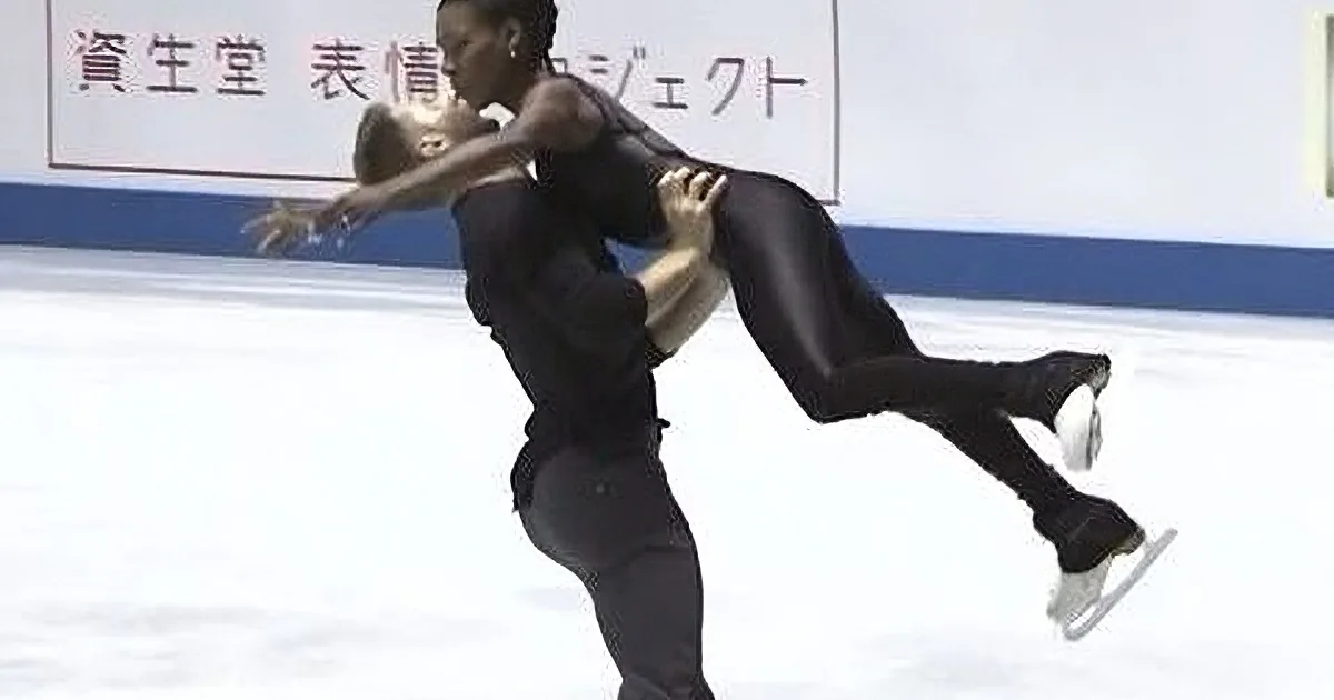 A figure skater in black lifts another skater mid-air during a performance on ice.