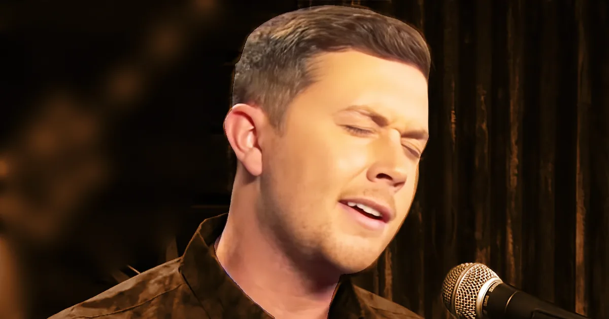 A man in a brown shirt sings into a microphone, eyes closed, in a dimly lit setting.
