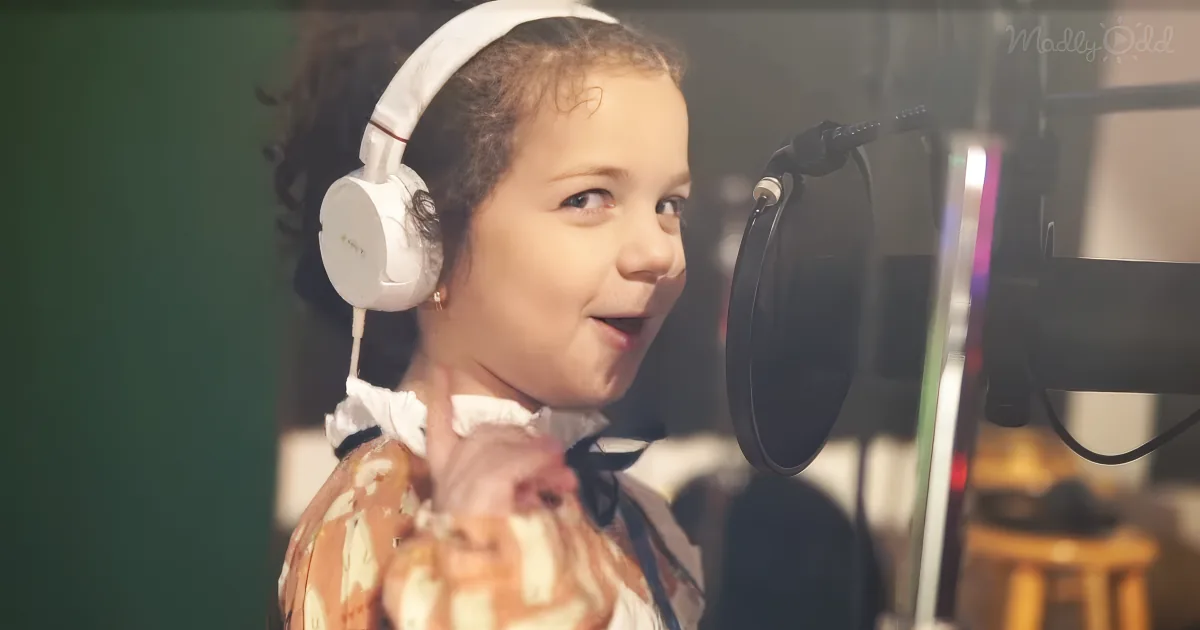 A child wearing headphones and a floral shirt is smiling near a microphone in a recording studio.
