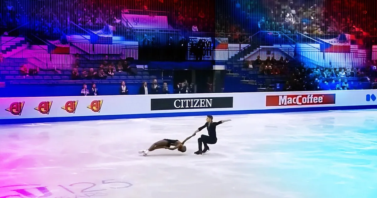 Two figure skaters perform a dramatic lift on ice, with one skater in a handstand and the other supporting them.