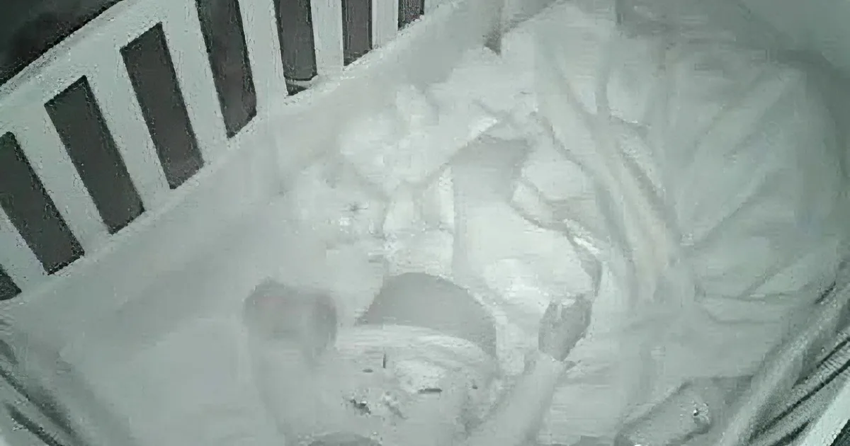 A baby is sleeping in a white crib with a white blanket and pillow.