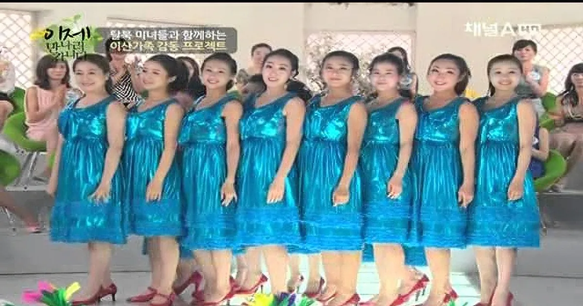 A group of women in matching blue dresses and red heels stand in a line, smiling.