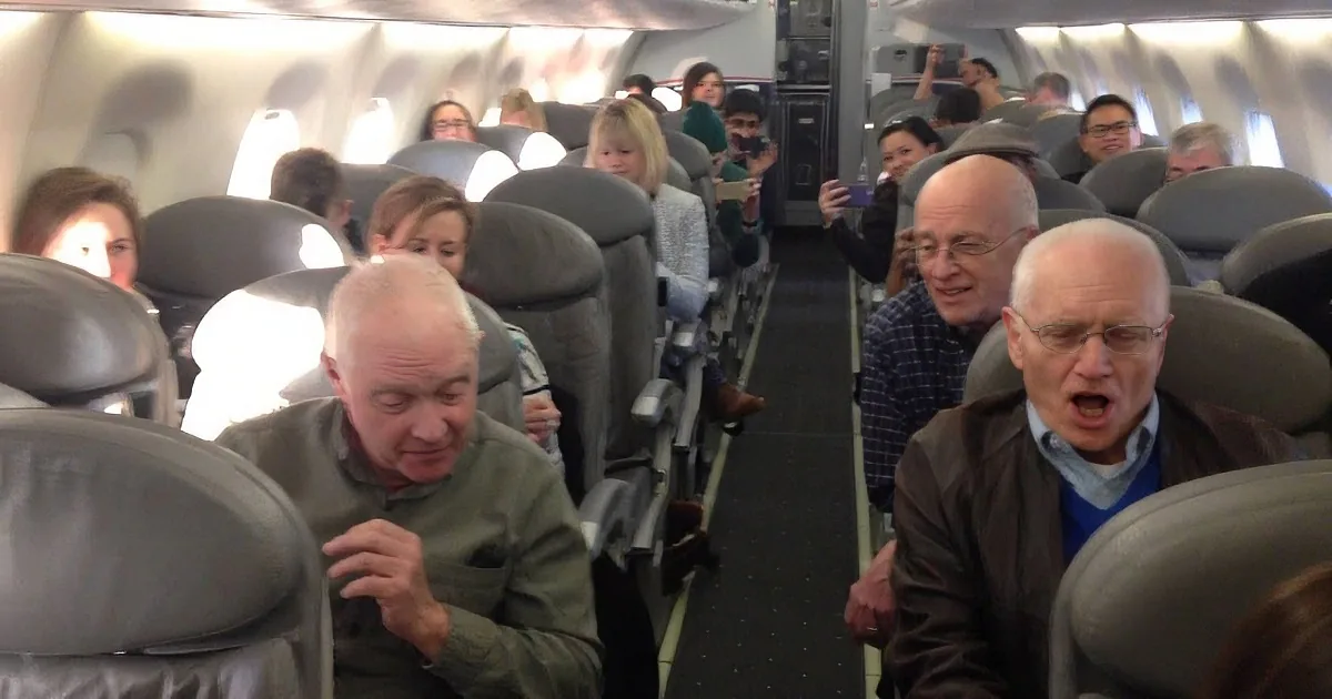 Passengers in an airplane cabin, some appearing tired or stressed, with overhead compartments open and seats tightly packed.