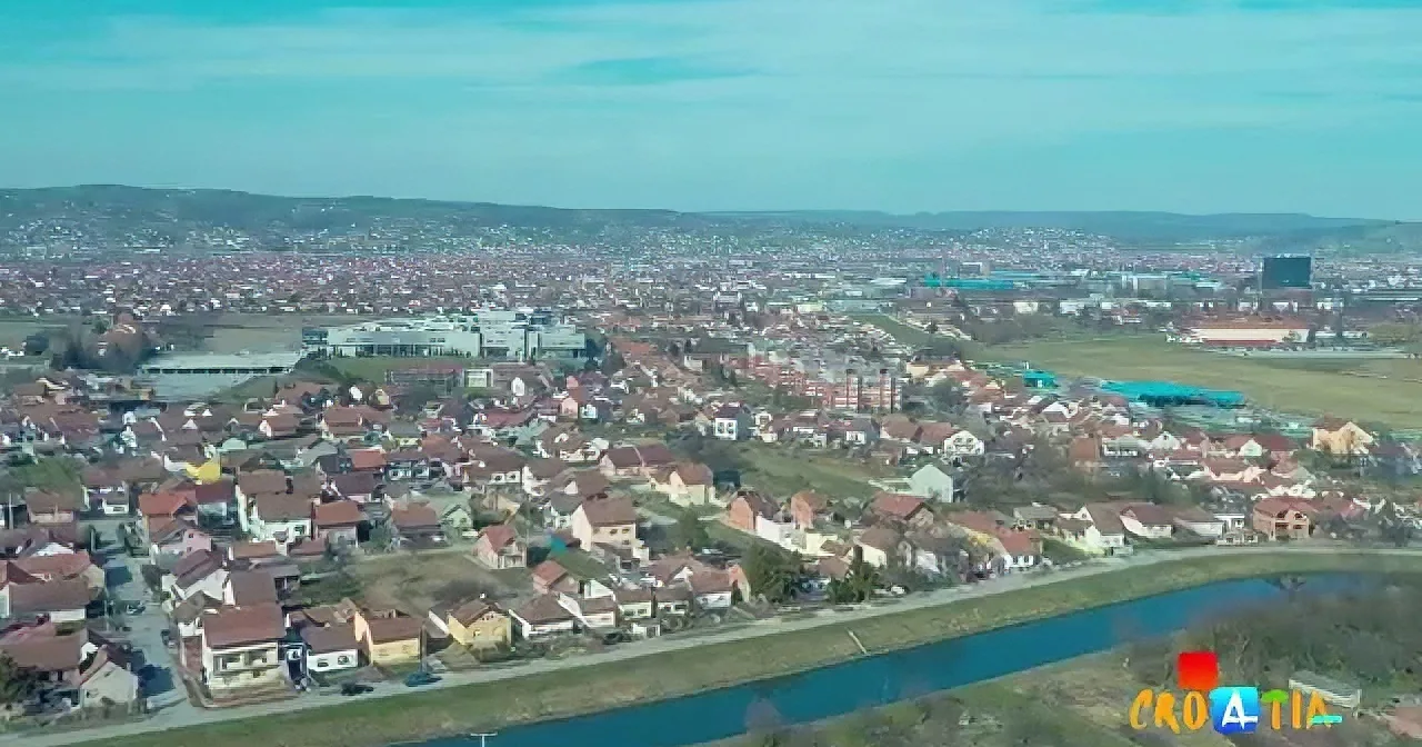 Aerial view of a densely populated area with houses, a river, and distant hills under a clear sky.