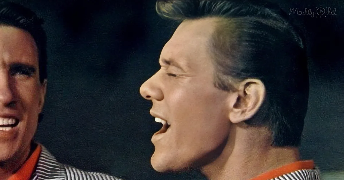 A man with a distinctive hairstyle and striped shirt is shown in profile, smiling widely.