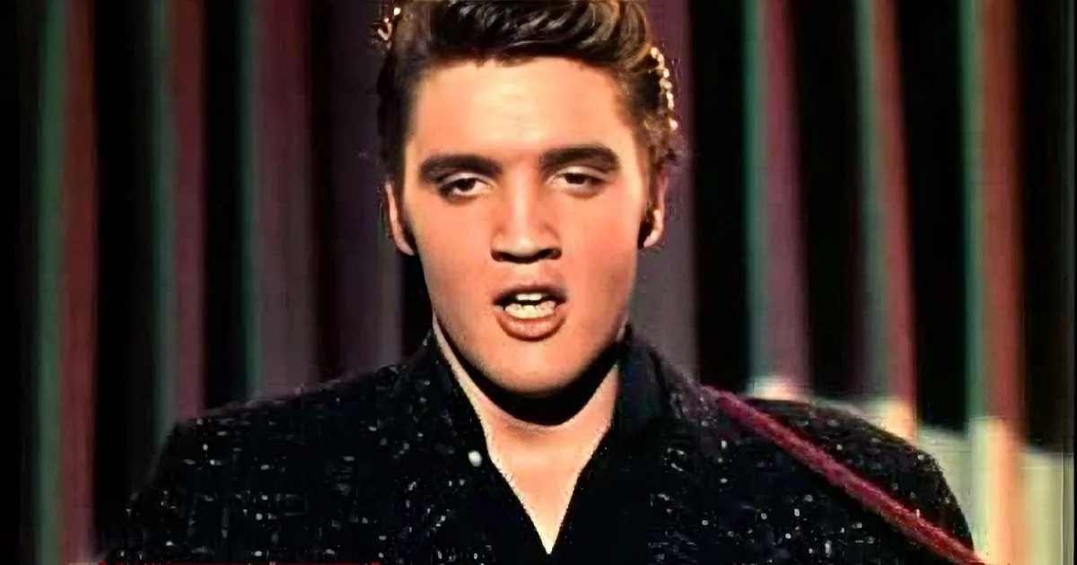 A man with styled hair and a black patterned shirt is singing, with a microphone visible.