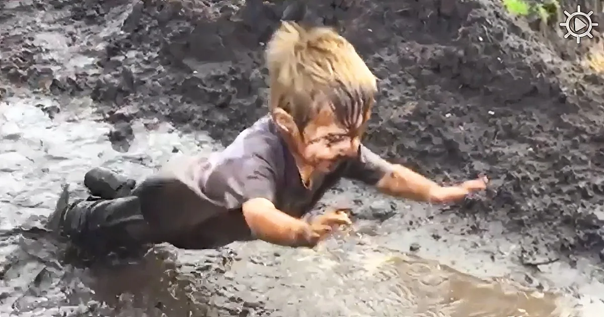 A person is crawling through a muddy area, wearing dark clothing and boots.