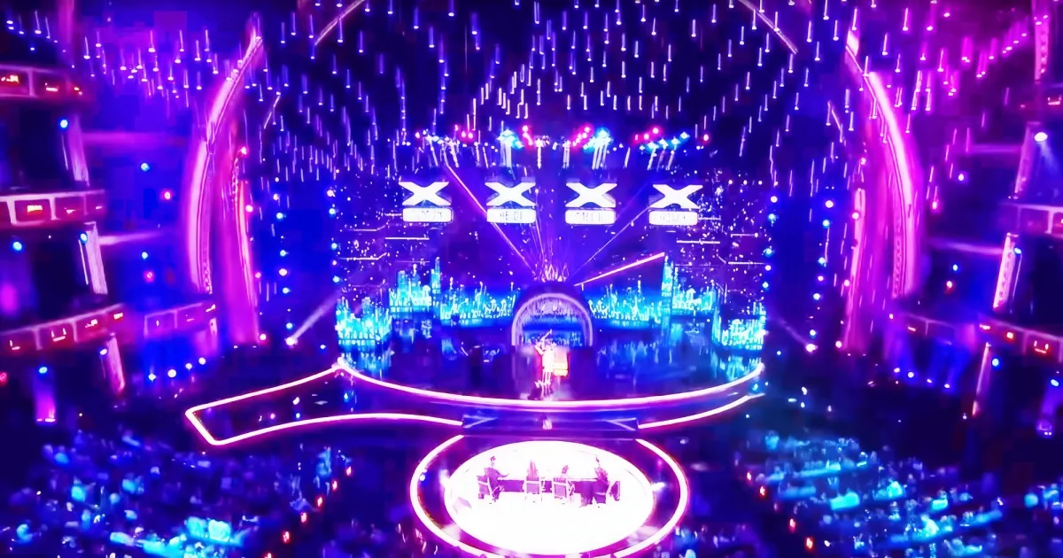 A vibrant concert stage with bright lights, a large screen, and a crowd in the foreground.