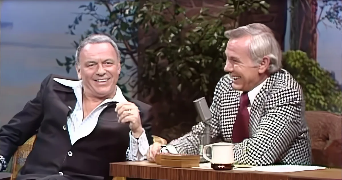 Two men in suits are seated at a table, smiling and laughing together.