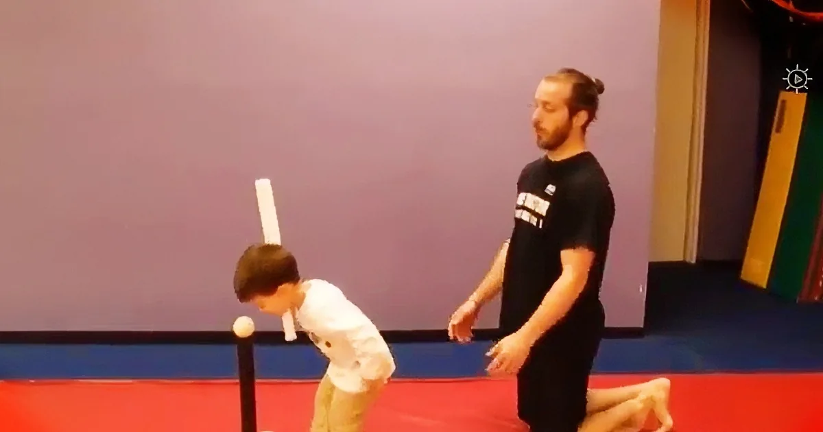 A young child practices a martial arts move with an adult instructor in a gym.