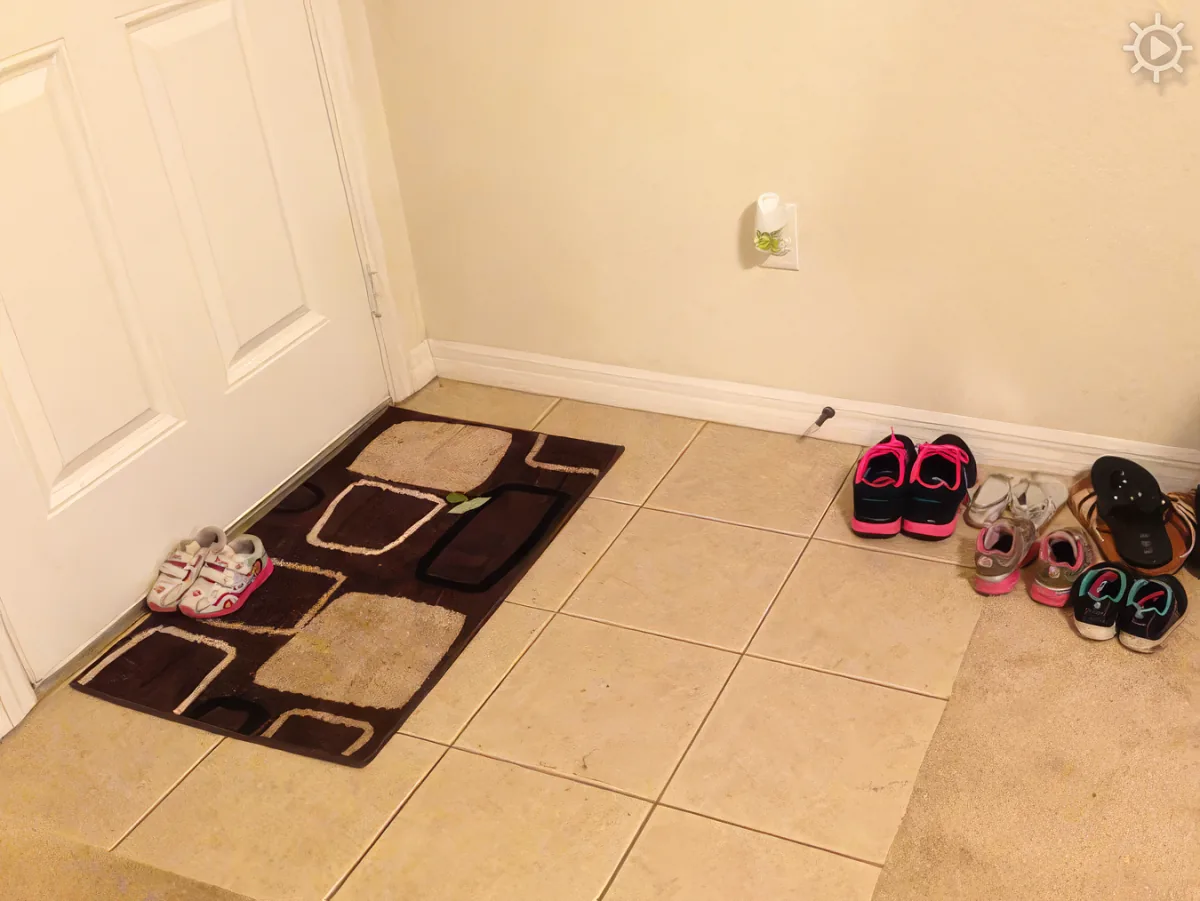 A tiled floor with a brown and beige rug, shoes, and a white door.
