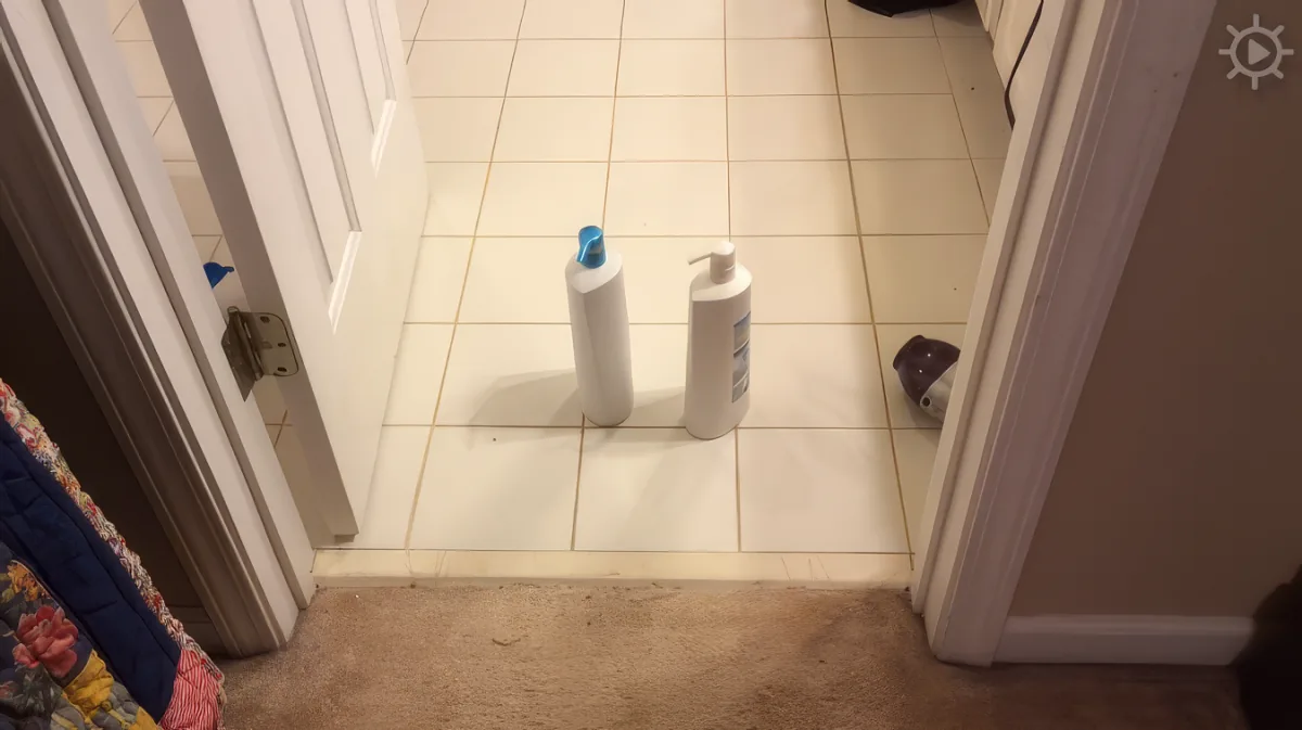 Two bottles, one with a blue cap, sit on a tiled bathroom floor near a doorway.
