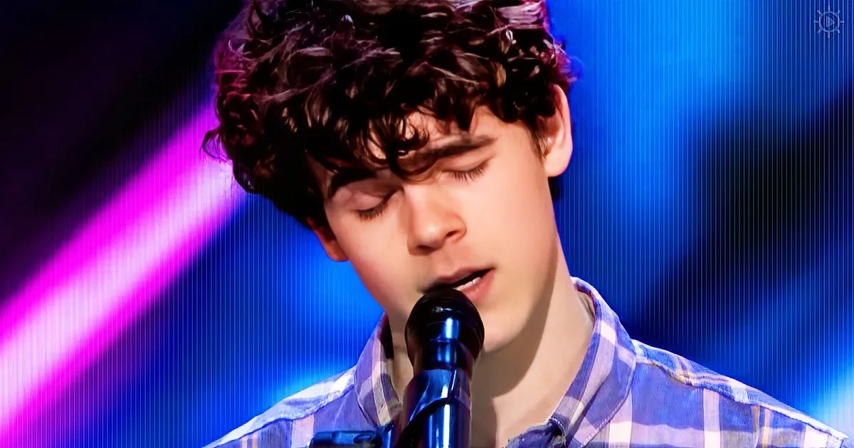 A young person with curly hair sings into a microphone, wearing a plaid shirt, against a blue and purple background.