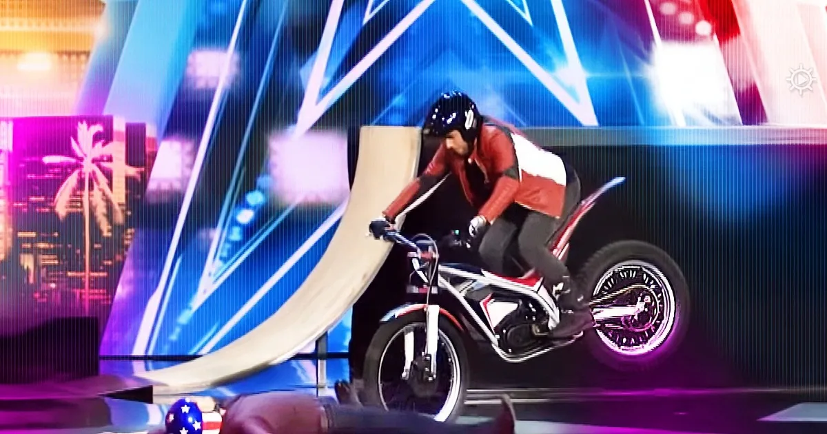 A person rides a stunt bike on a ramp, performing a trick on a stage with colorful lights.