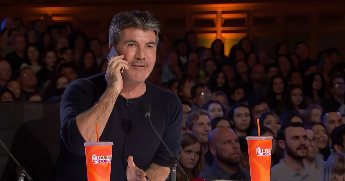 Simon Cowell is on a phone call, surrounded by audience members and Dunkin' Donuts cups.