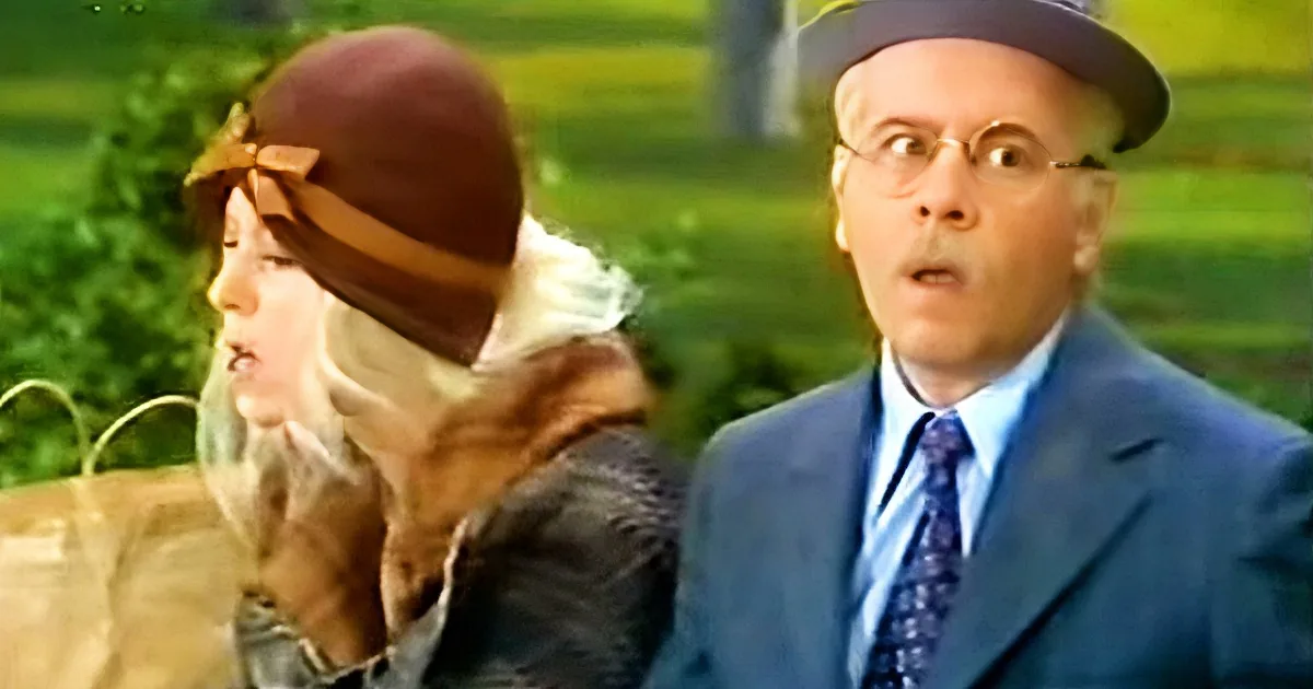 A man in a blue suit and hat appears surprised, while a woman in a brown hat and scarf looks on.