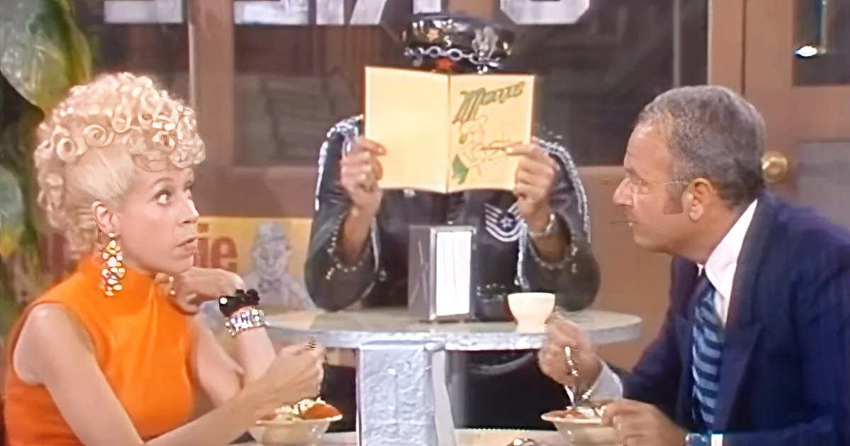 A woman in an orange dress sits at a table with a man in a suit, holding a menu.