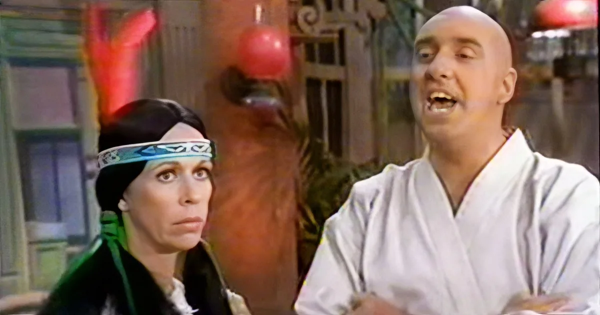 A person in a white robe is laughing, while another person in a green outfit looks on with a concerned expression.