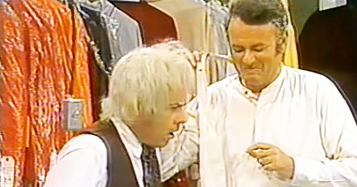 An older man in a white shirt and tie is looking down, possibly at a phone, while another person with white hair and...