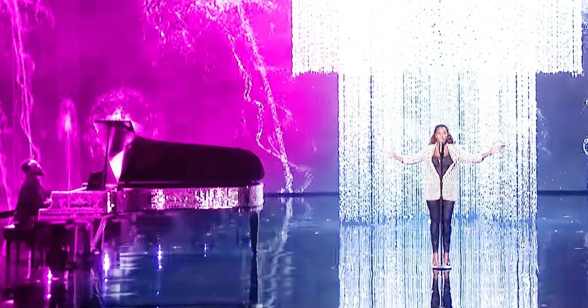 A woman stands on a platform surrounded by cascading lights, with a pianist playing in the background.