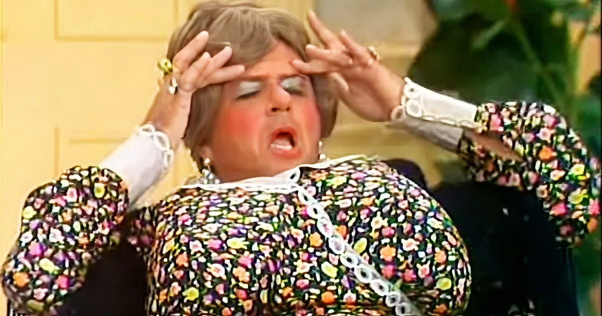 A woman in a floral dress holds her head with both hands, appearing distressed.