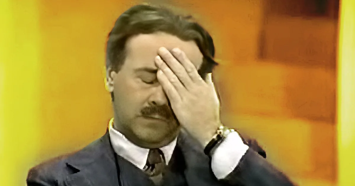 A man in a suit and tie covers his face with his hand, appearing distressed.
