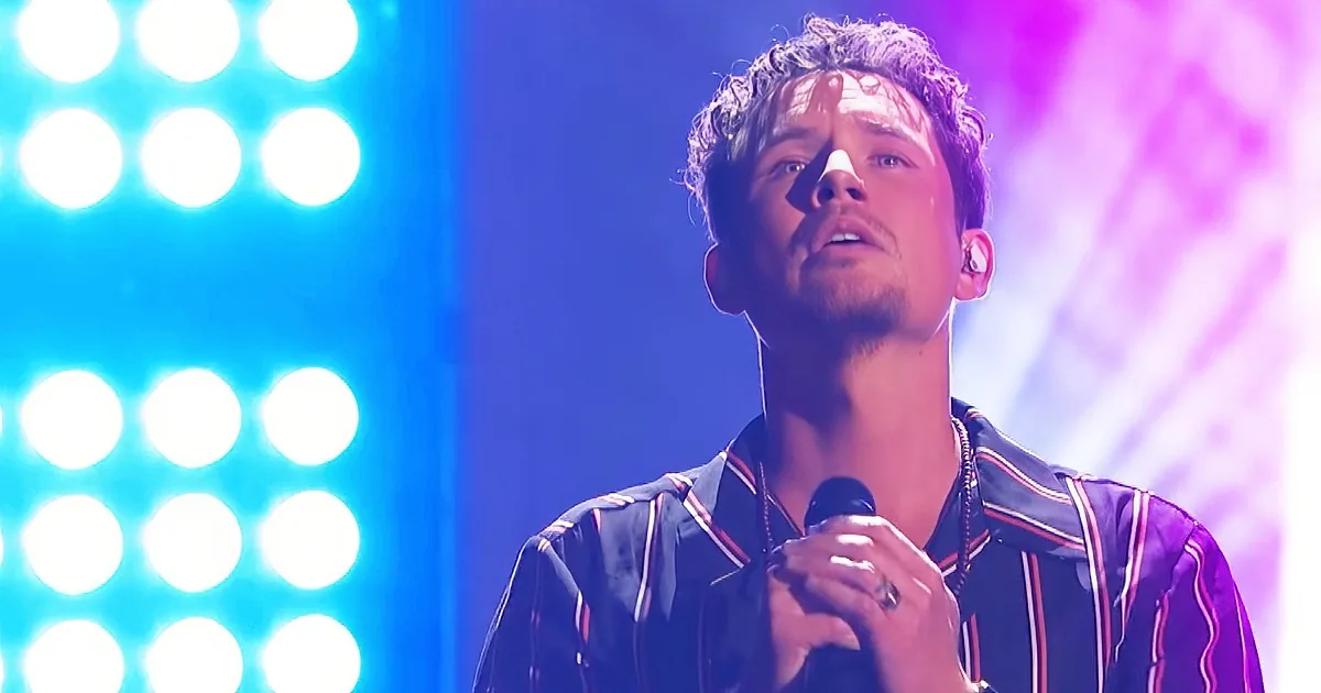 A man in a striped shirt holds a microphone, singing under vibrant blue and purple stage lights.