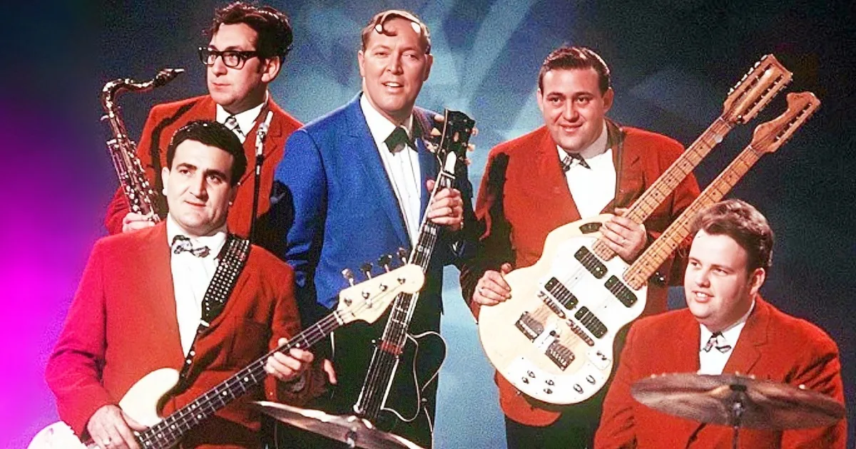 A band in red suits with guitars and a saxophone, posing on stage with a vibrant background.