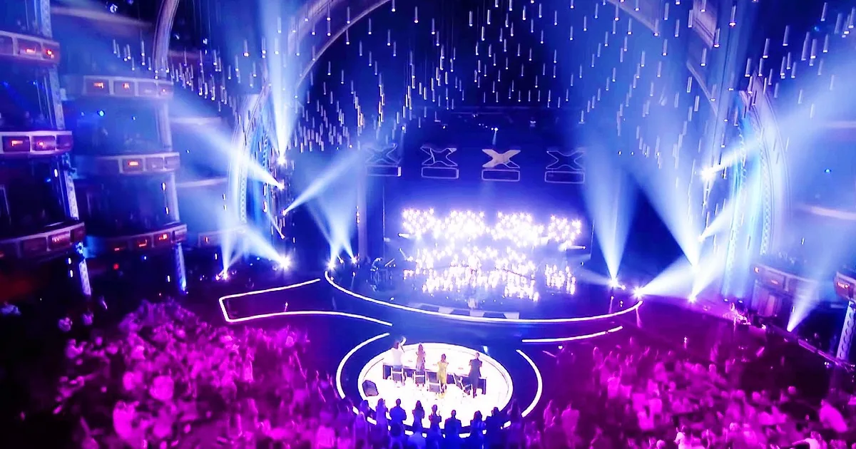 A vibrant concert scene with a large crowd, bright stage lights, and performers on a raised platform.