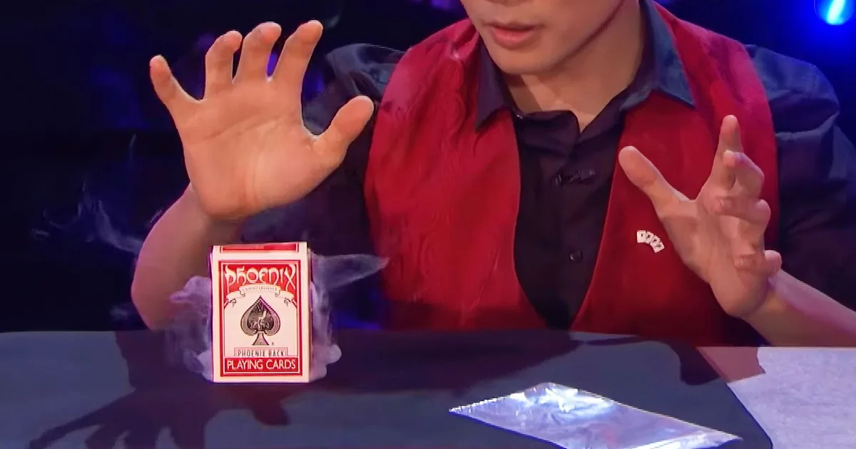 A magician in a red vest performs a card trick with a deck of Phoenix Playing Cards on a table.