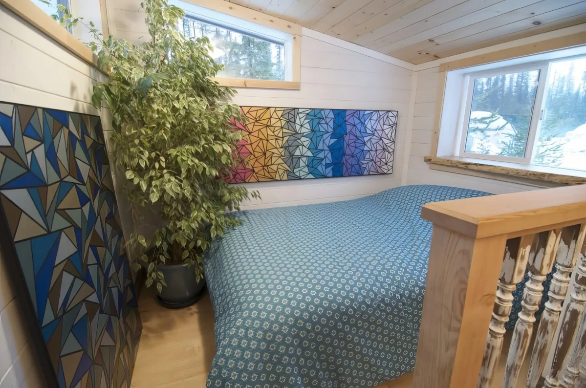 A cozy bedroom with a blue patterned bed, wooden walls, and colorful geometric wall art.