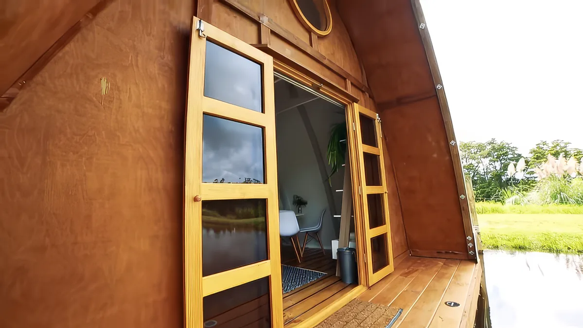 A wooden cabin with open doors reveals a cozy interior, featuring a chair and a small table, set against a backdrop of...