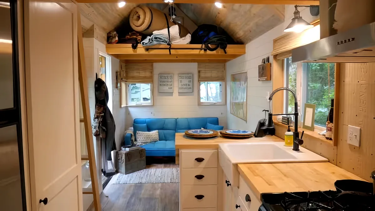 A cozy, compact kitchen with wooden cabinets, a sink, and a blue couch in the background.