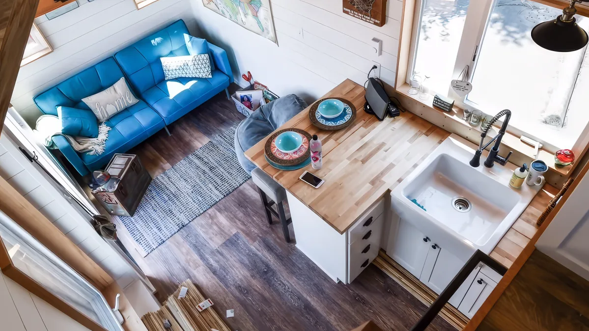 A cozy, compact living space with a blue sofa, wooden countertop, and white sink in a tiny home.