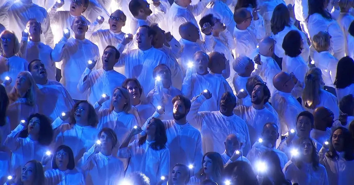 A choir in white robes sings with glowing lights in their hands, creating a luminous effect.